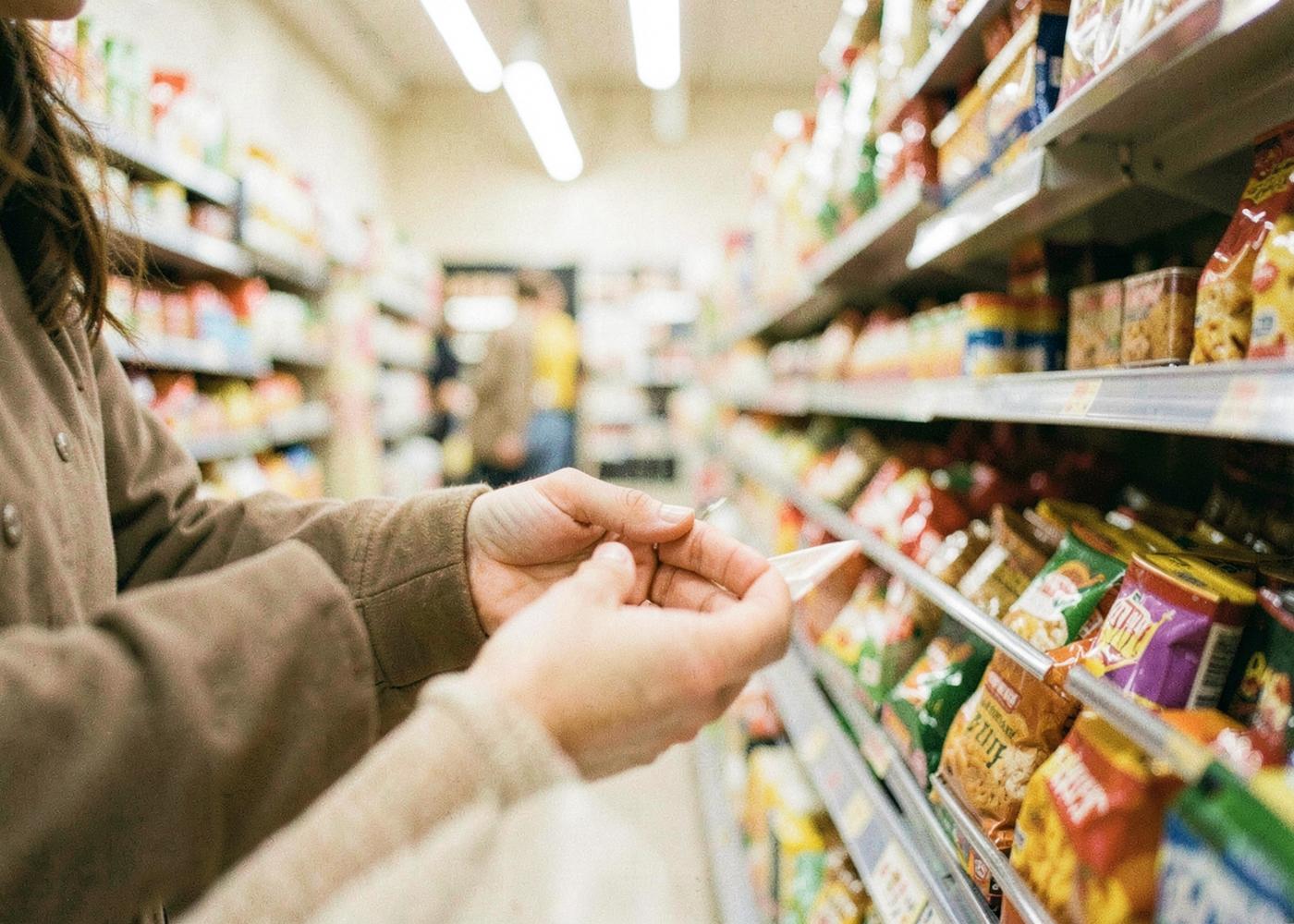 A shopper's hands examining a product in a supermarket aisle